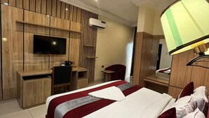 Une chambre d’hôtel avec un grand lit, un bureau avec une chaise, un téléviseur fixé au mur et un appareil de climatisation.
