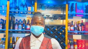 Une personne se tient devant un bar dont les étagères sont remplies de bouteilles.