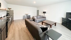 A modern living room with a sofa, coffee table, and a dining area with stools.