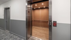 An elevator with a metallic exterior, a wooden interior, and a control panel with a red emergency button.