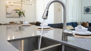A modern kitchen with a stainless steel sink, a faucet, and a dining area with a table set for two. - BRAND-NEW 4BD/3BTH Townhome near Disney #141 (Kissimmee)