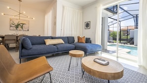 A modern living room with a sectional sofa, a coffee table, and a dining area with chairs and a table. - BRAND-NEW 4BD/3BTH Townhome near Disney #141 (Kissimmee)
