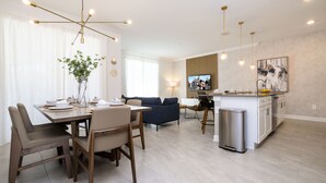 A modern living room with a dining area, a sofa, and a kitchen with a TV. - BRAND-NEW 4BD/3BTH Townhome near Disney #141 (Kissimmee)