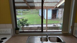Una cocina con un lavamanos de acero inoxidable, estufa y ventana con vista a un jardín.
