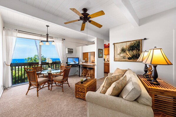 A spacious living area with a balcony, a dining table with chairs, a sofa, a ceiling fan, and a painting on the wall.