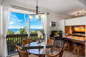 A dining area with a glass table, wicker chairs, and a view of the ocean.