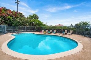 A swimming pool with a curved edge, surrounded by a fence, and several lounge chairs.
