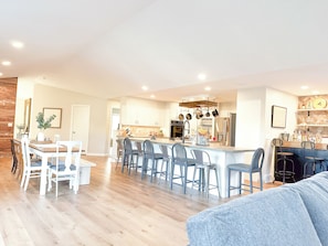 A spacious kitchen with a central island, bar stools, and a dining area with white chairs. - The Attic: Sandusky’s Premier Group & Sports Team Stay (Sandusky)