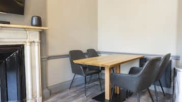 Un comedor con una mesa de madera y cuatro sillas, una chimenea y un televisor montado en la pared.