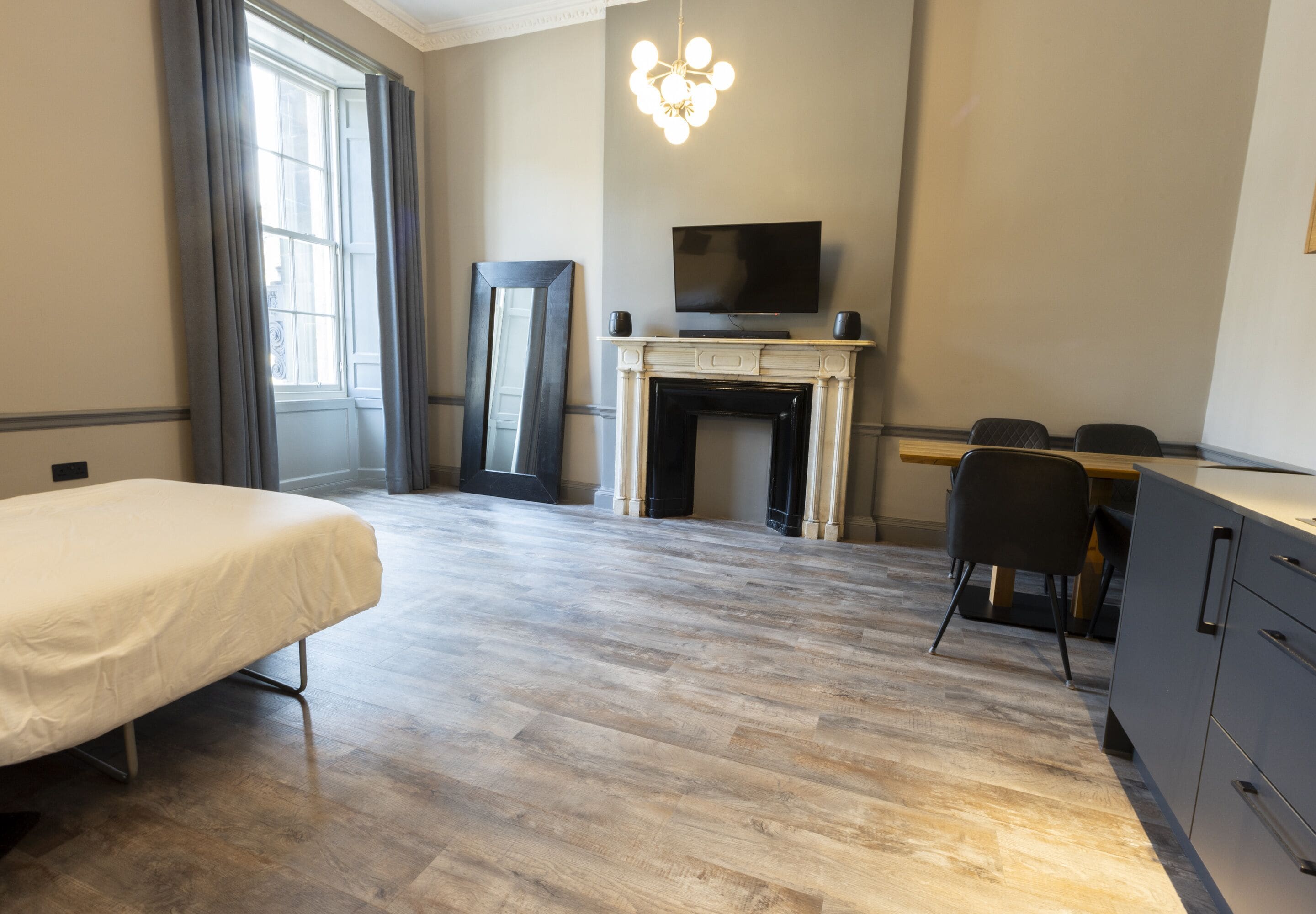 A hotel room with a bed, a TV on a mantelpiece, a fireplace, and a desk with chairs.