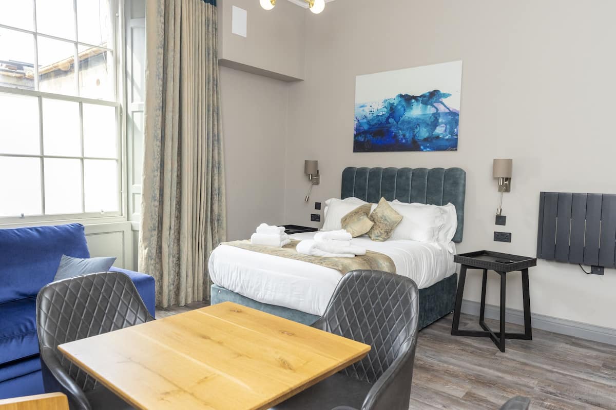 A hotel room with a bed, a wooden table, a blue sofa, and a painting on the wall.