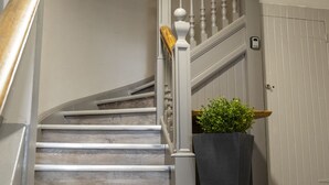 Un escalier avec des marches en bois et des rampes blanches, menant à un palier où se trouve un pot de fleurs.