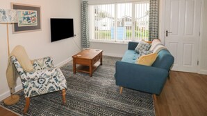 Ein Wohnzimmer mit einem blauen Sofa, einem gemusterten Sessel, einem Holztisch und einem großen Fenster mit Vorhängen.