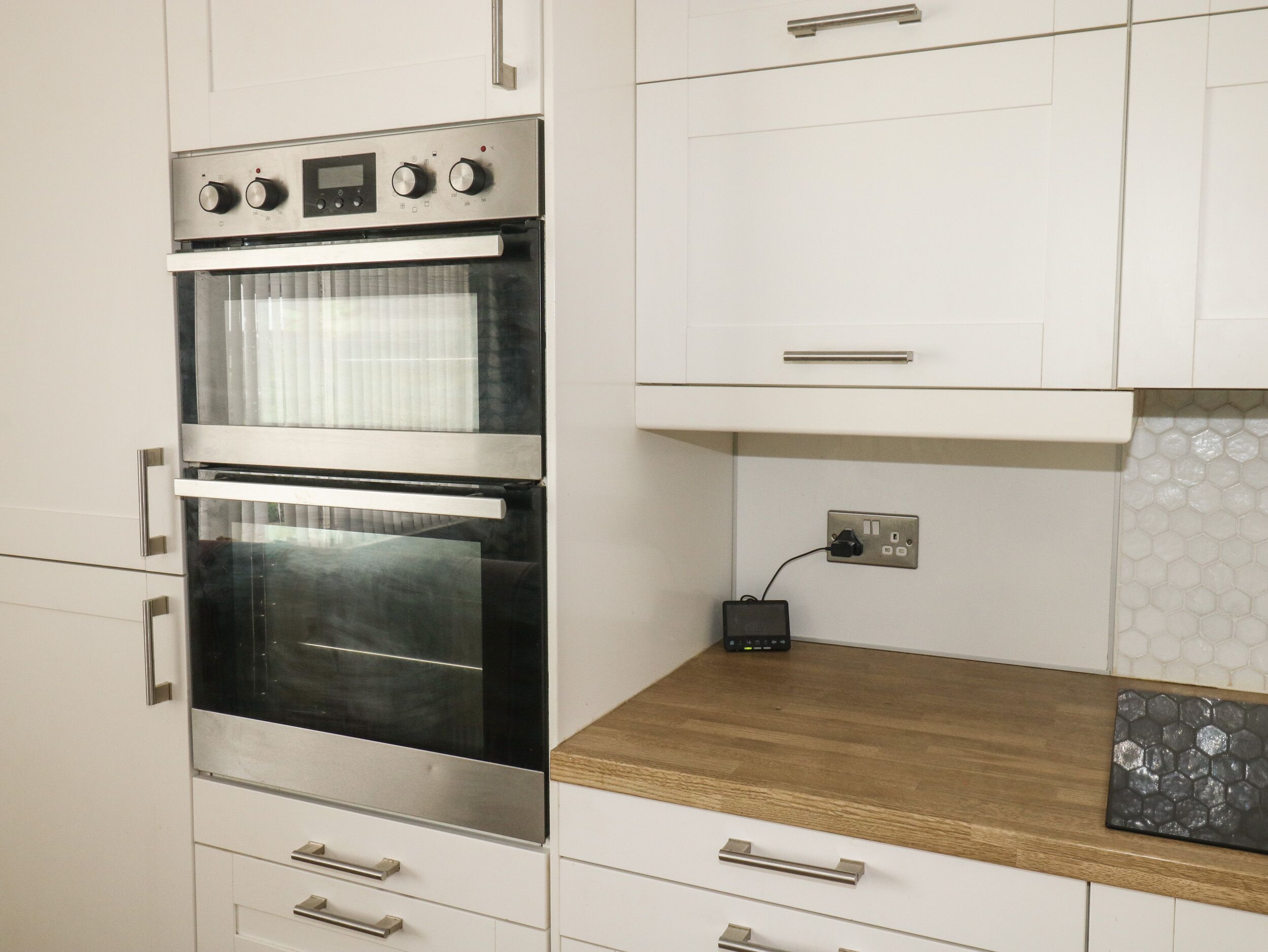 Cozinha moderna com eletrodomésticos de aço inoxidável, armários brancos e bancada de madeira.