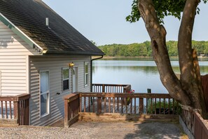 Overlooking a serene body of water, this cabin features a cozy front porch with a seating area and a large tree providing shade.