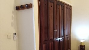 A room with a large wooden wardrobe, a green metal rack, and a small bedside table with a lamp. - Magic Building Apartment 4 (Tarrafal)