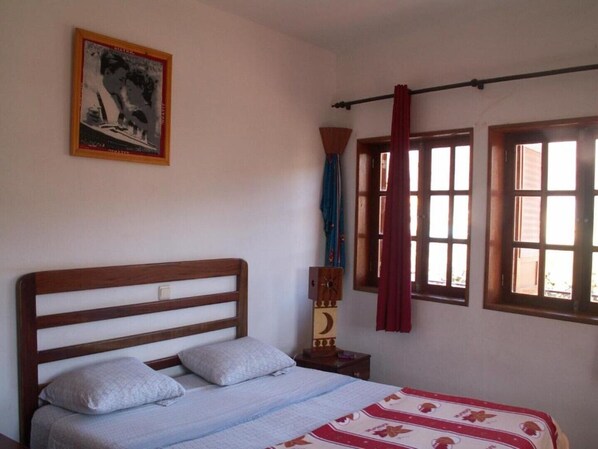 A bedroom with a wooden bed, a nightstand, a wall-mounted clock, and a window with curtains.