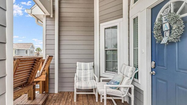 A porch with two white wicker chairs and a wooden bench, a blue door with a wreath, and a view of neighboring houses. - Trinity Tides, the waves dance, and so do your worries (Port Aransas)