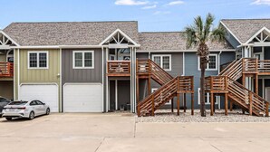 A row of townhouses with attached garages, wooden staircases, and a palm tree in the foreground. - Trinity Tides, the waves dance, and so do your worries (Port Aransas)