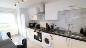 Une cuisine moderne avec des meubles blancs, un four encastré, un lave-linge et un évier.