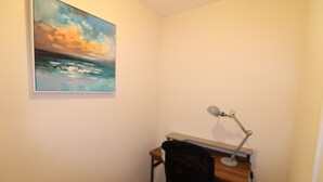 Un petit bureau comprenant un bureau, une chaise et un tableau représentant un paysage marin.