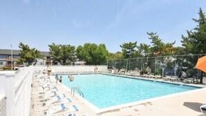 Una piscina con sillas de descanso y sombrillas, rodeada de árboles y edificios.