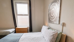 Une chambre à coucher avec un lit, une fenêtre, une œuvre d’art accrochée au mur et une lampe de chevet.