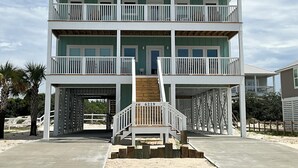 Uma casa de praia de dois andares com varanda em cada andar, uma entrada coberta e o número '619' exibido.