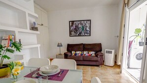 Een eethoek met een tafel gedekt voor twee personen, een bank, een wanddecoratie, en uitzicht op een wasmachine door een geopende deur.