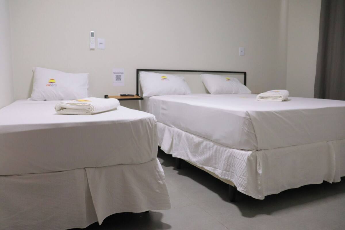 Two single beds with white bedding and towels, a control panel, and a small table with a remote control.