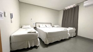 A hotel room with two single beds, a bedside table, a wall-mounted phone, and an air conditioning unit. - Fly Hotel (Varzea Grande)