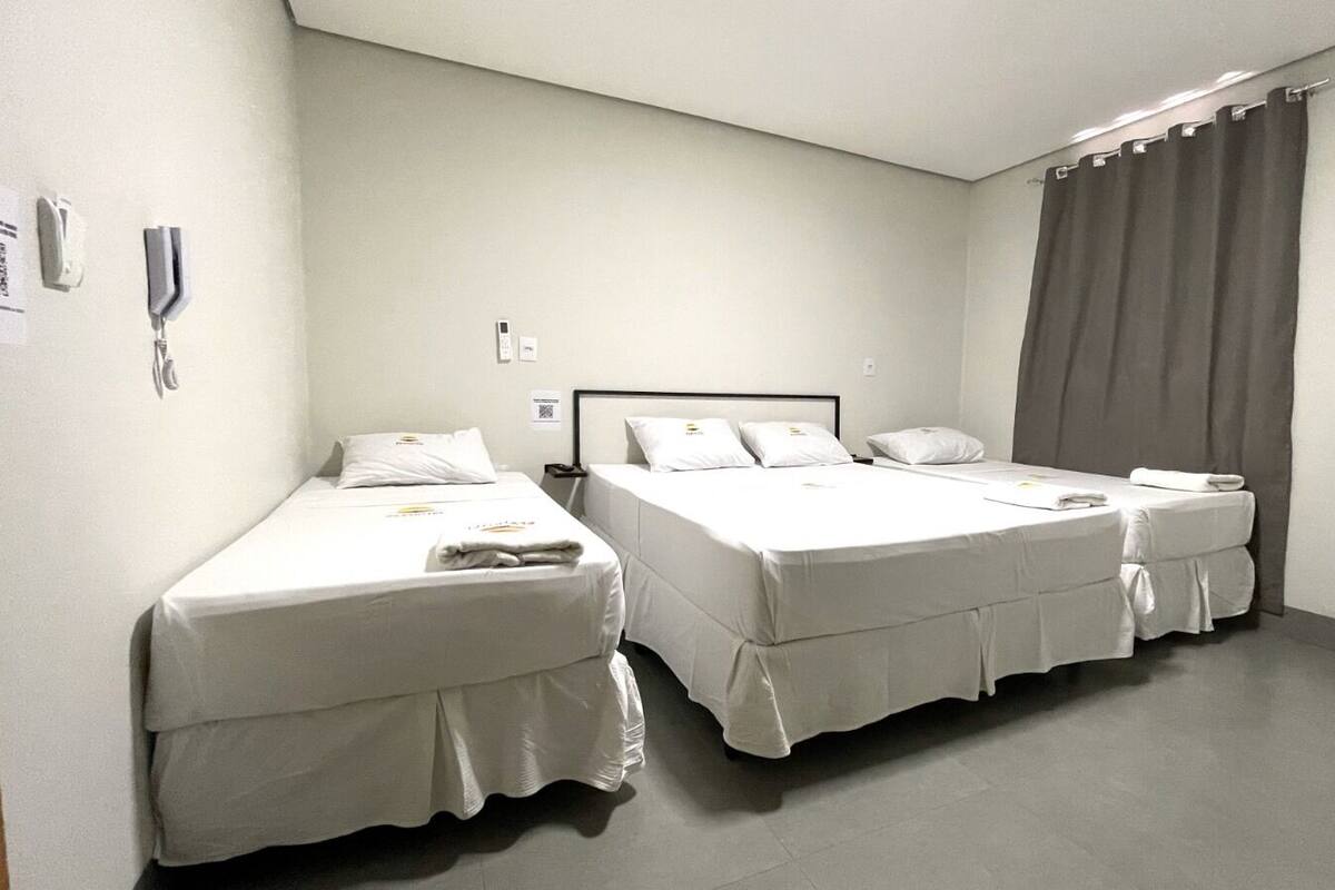 A hotel room with two single beds, a bedside table, a wall-mounted phone, and an air conditioning unit.