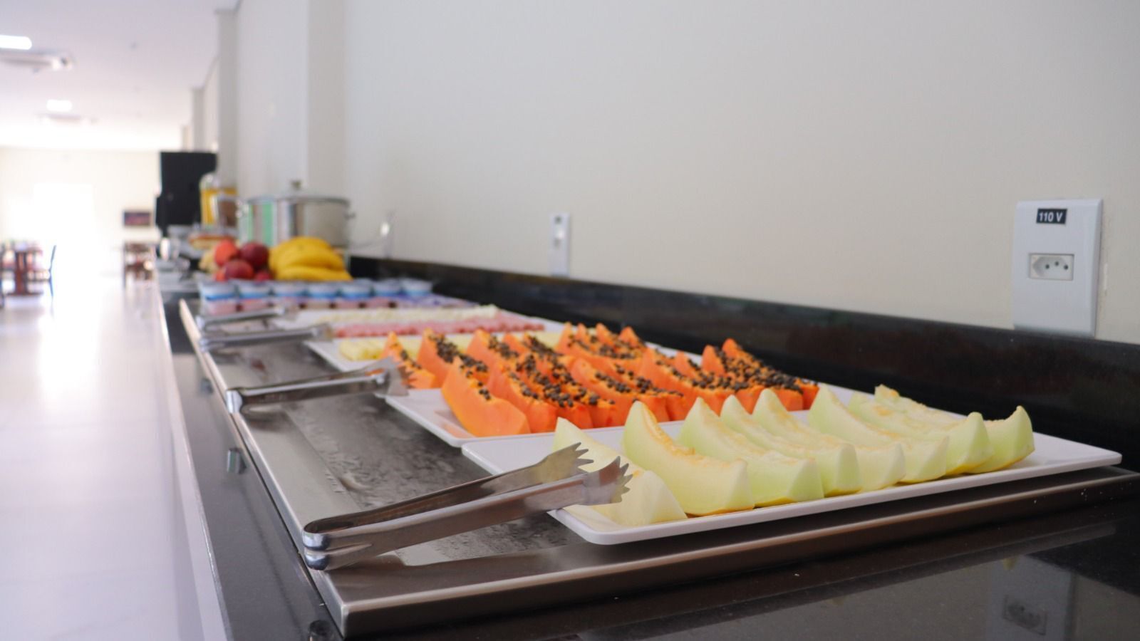 Una barra de buffet con frutas y verduras variadas, incluyendo papaya y melón, sobre una encimera negra.