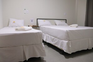 Habitación de hotel con dos camas individuales, cada una con cubrecama y almohadas blancas, y una toalla doblada sobre la cama.