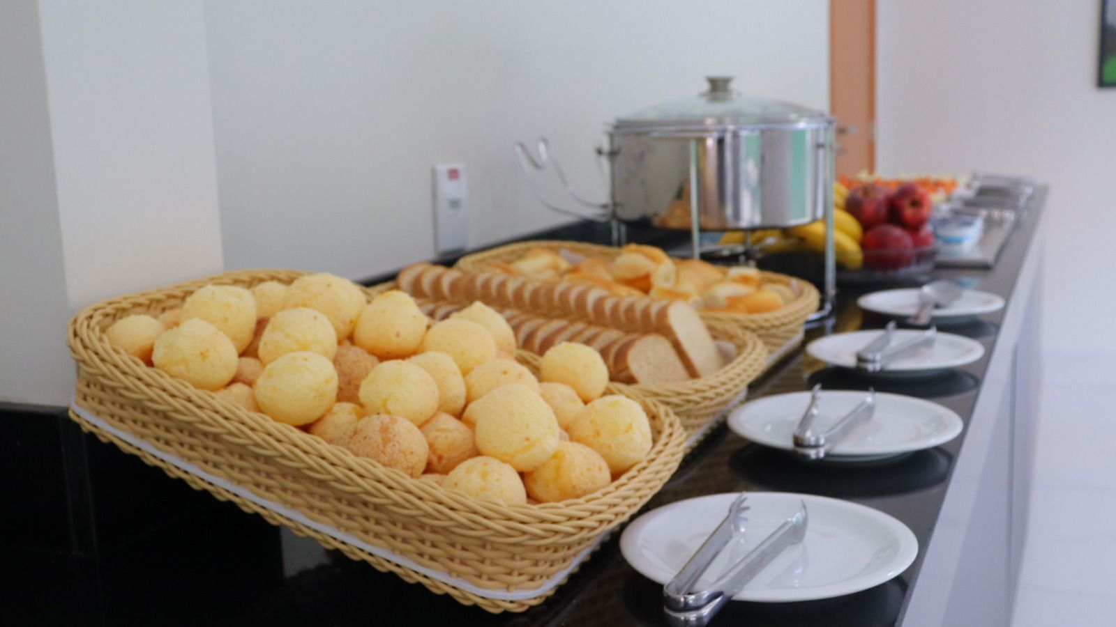 A buffet table with baskets of bread and pastries, a pot on the stove, and plates with utensils.
