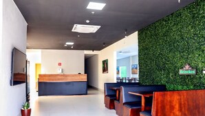 A modern reception area with a green wall, wooden reception desk, and seating area. - Fly Hotel (Varzea Grande)