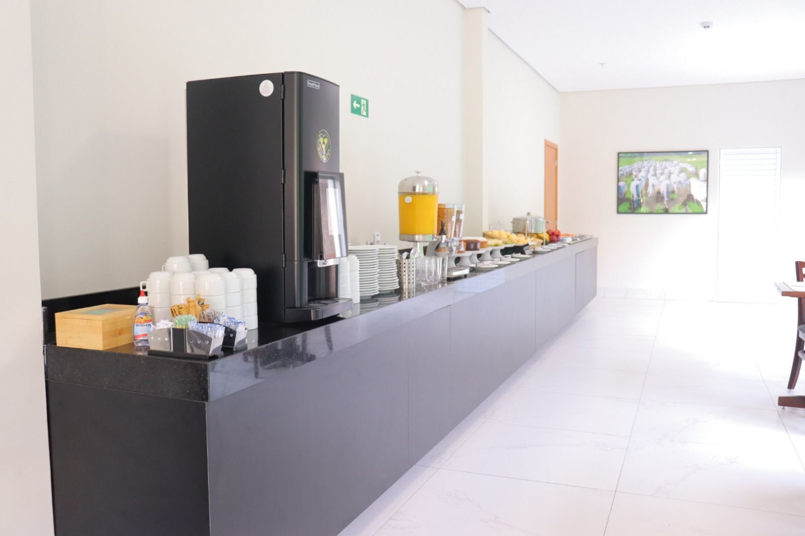 A long counter with a coffee machine, a juice dispenser, and various food items.