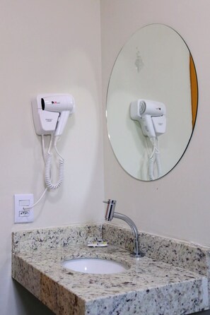 A bathroom with a granite countertop sink, a mirror, and two hair dryers mounted on the wall. - Fly Hotel (Varzea Grande)