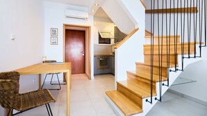 Ein modernes Interieur mit einer Holztreppe, einem Essbereich mit Tisch und Stühlen sowie einer Küche im Hintergrund.