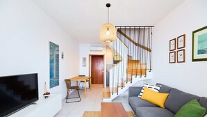 Ein modernes Wohnzimmer mit einem Flachbildfernseher, einem grauen Sofa mit gelben und grünen Kissen, einem Holztisch und einer Treppe mit einem Holnlaufgeländer.