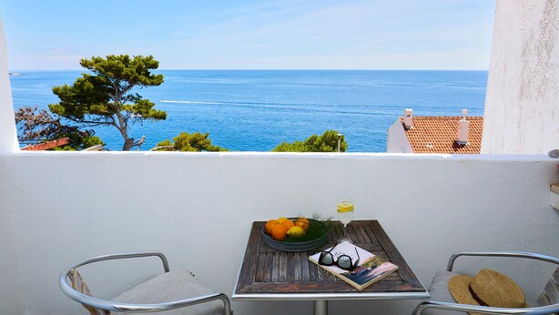 Ein Balkon mit Blick aufs Meer, ein Tisch mit Obstschale, ein Getränk in einem Glas und eine Sonnenbrille.