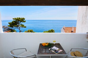 Un balcon avec vue sur la mer, une table avec un panier de fruits, un verre et une paire de lunettes de soleil.