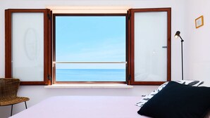 Ein Schlafzimmer mit Bett, einem Fenster mit Meerblick, einem Sessel und einer Stehlampe.