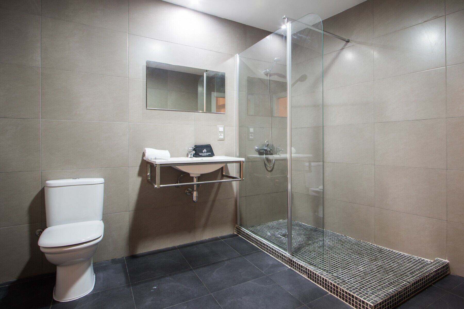 A modern bathroom with a toilet, a sink with a towel, and a glass-enclosed shower.