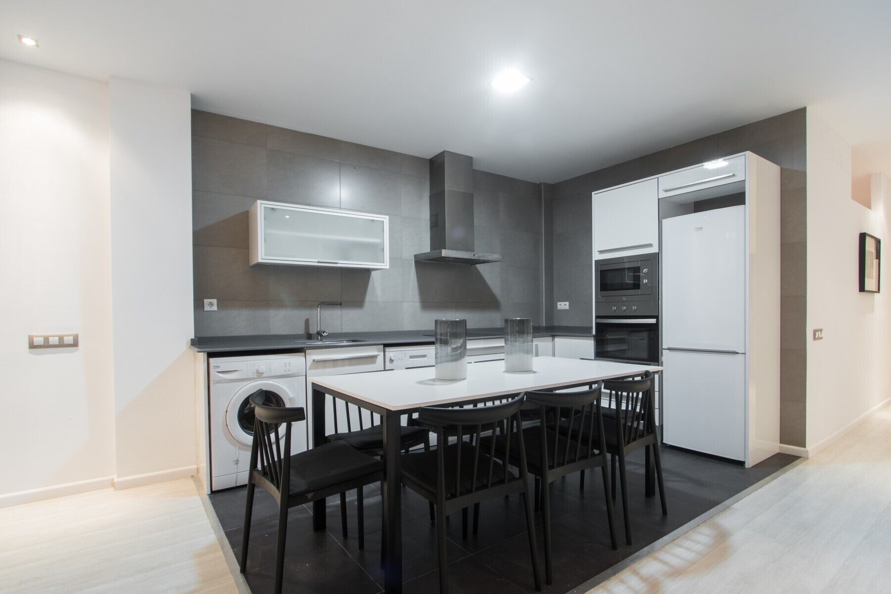 Een moderne keuken met een ingebouwde oven, magnetron en vaatwasser, een eettafel met stoelen en een wasmachine.