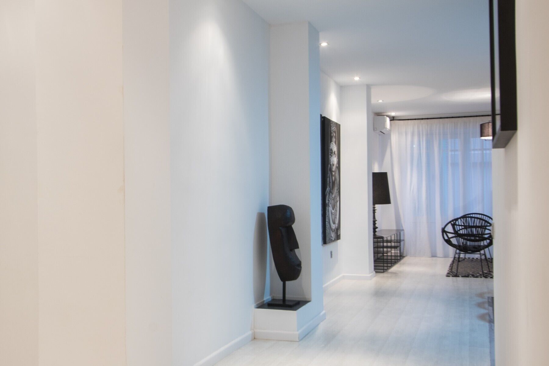 Ein moderner Flur mit minimalistischem Design, mit einem hellen Boden, einer schwarzen abstrakten Skulptur und einem schwarzen Stuhl mit Metallgestell.