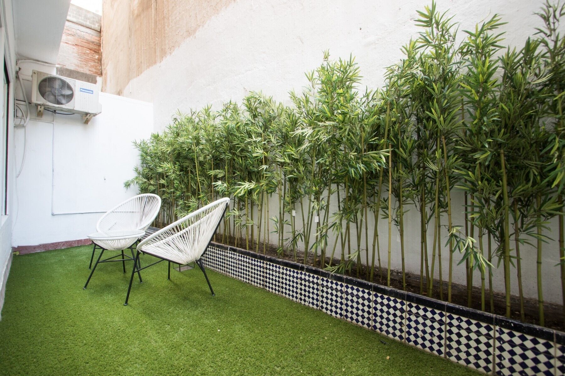 A small outdoor area with artificial grass, a white chair, and a bamboo fence.