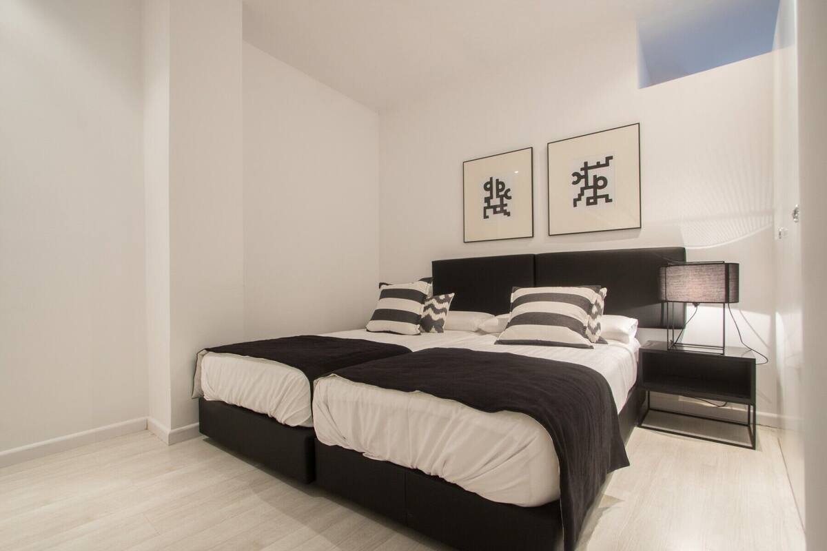 Een moderne slaapkamer met een zwart-wit bed, twee nachtkastjes en minimalistische inrichting.