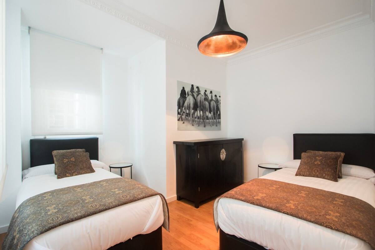 Een hotelkamer met twee bedden, een donker houten kast, een aan de muur hangend schilderij en een hanglamp.
