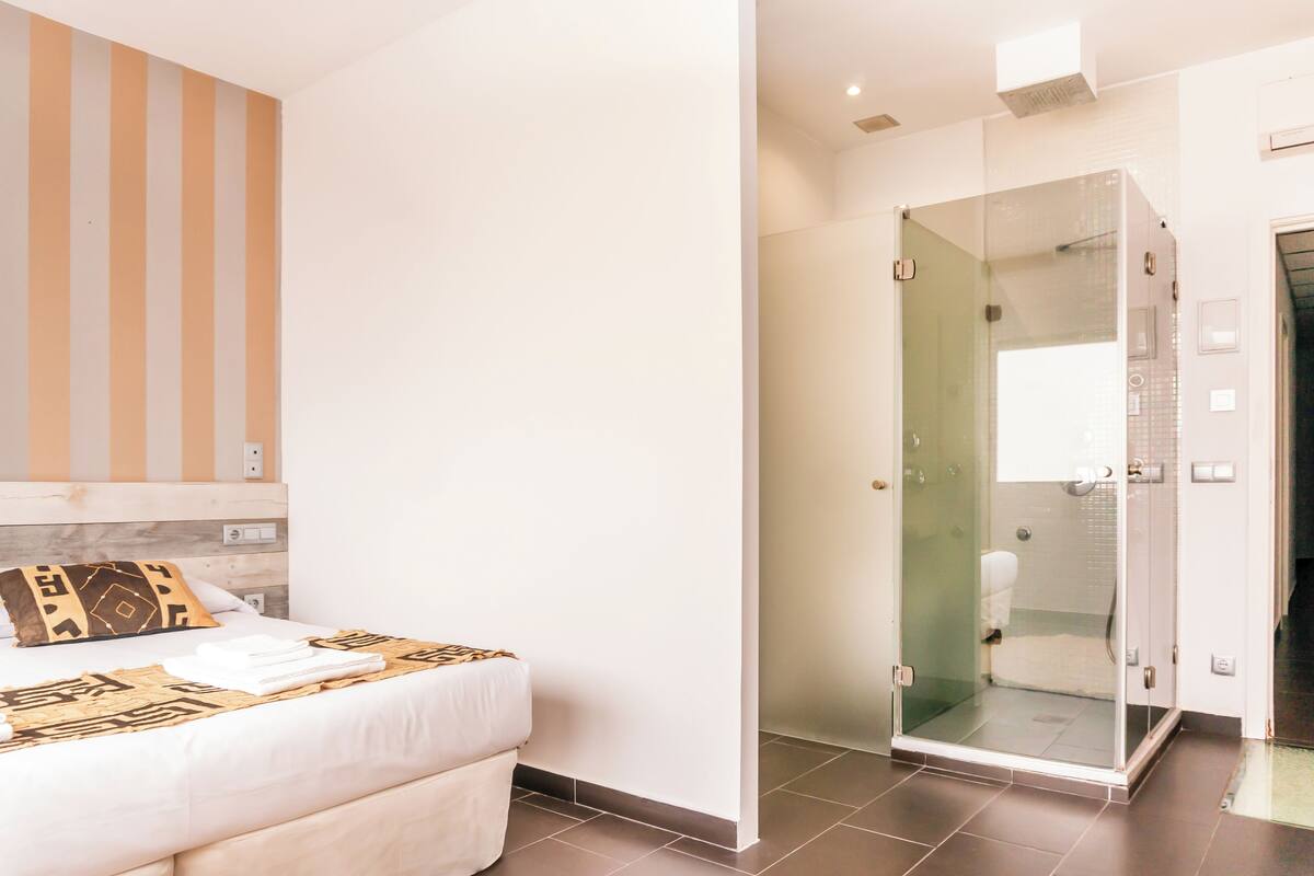 Een hotelkamer met een bed, een douchecel met glazen deuren en een gestreepte wand.